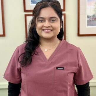 Dr. Krupa Patel smiling in mauve colored scrubs in a dental office setting